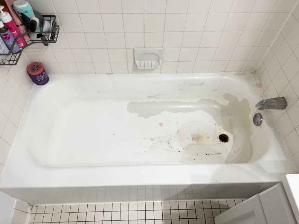 Expert Review: Common Failures of Spray-On Bathtub Coatings in Real-Life Use 2 The first image shows the condition of the tub after just two months. The coating is peeling in multiple areas, especially around the drain. Dirt has accumulated where the coating lifted, and discoloration is visible along the tub floor.